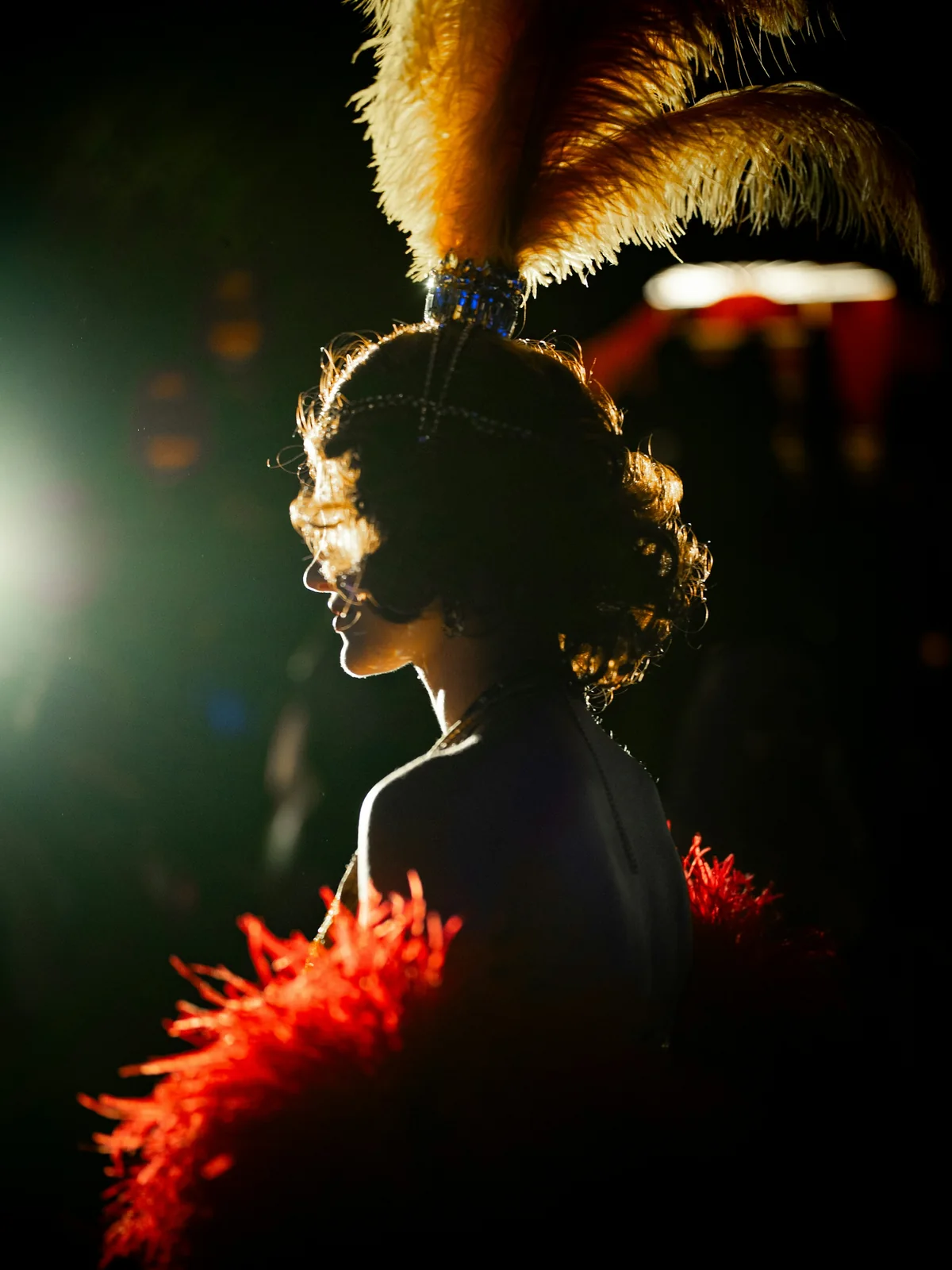 Silhouette of a performer wearing a feathered headdress and a red boa, lit from the side at night