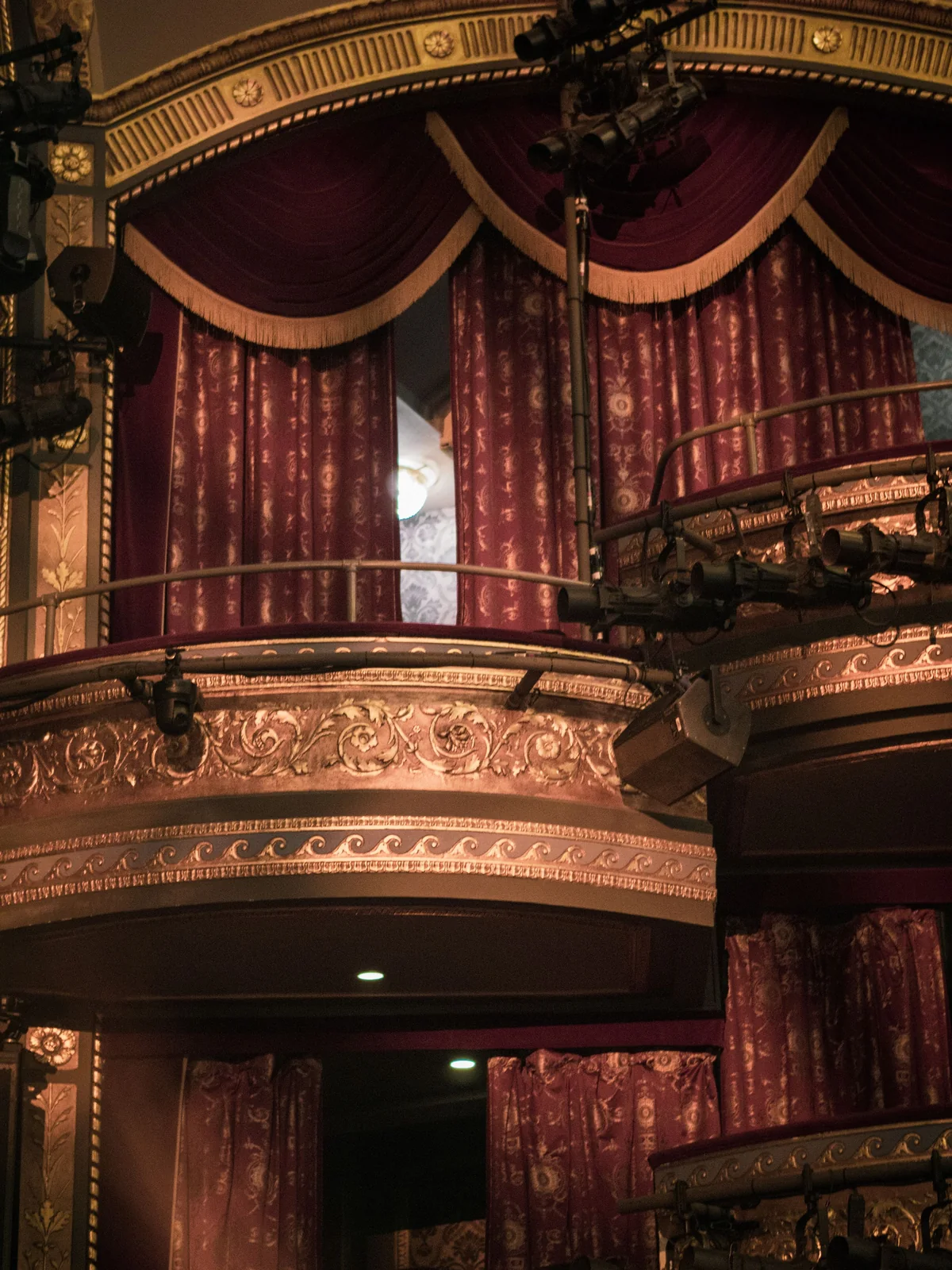 An ornate theatre balcony with red velvet drapery and gilded plasterwork