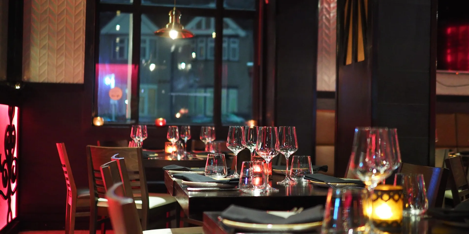 A dimly lit restaurant interior set with wine glasses and candles at each table